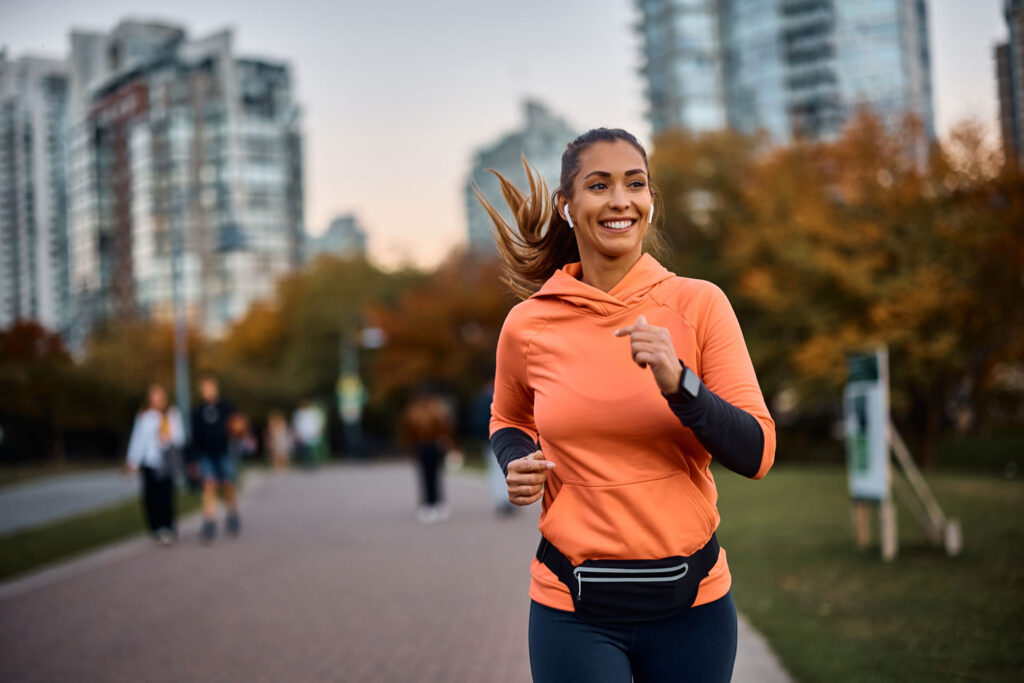 A smiling woman jogging outdoors on a sunny day, looking energized and refreshed after receiving a B12 shot.